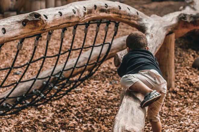 Boy playing outdoors on tree log outside space for kids